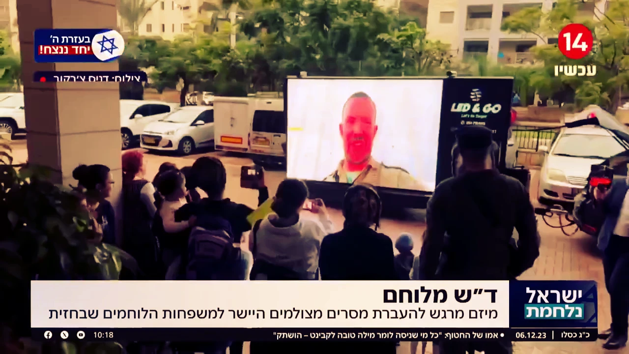 משפחות עומדות בשטח פתוח וצופות במסך LED נייד באירוע חוץ